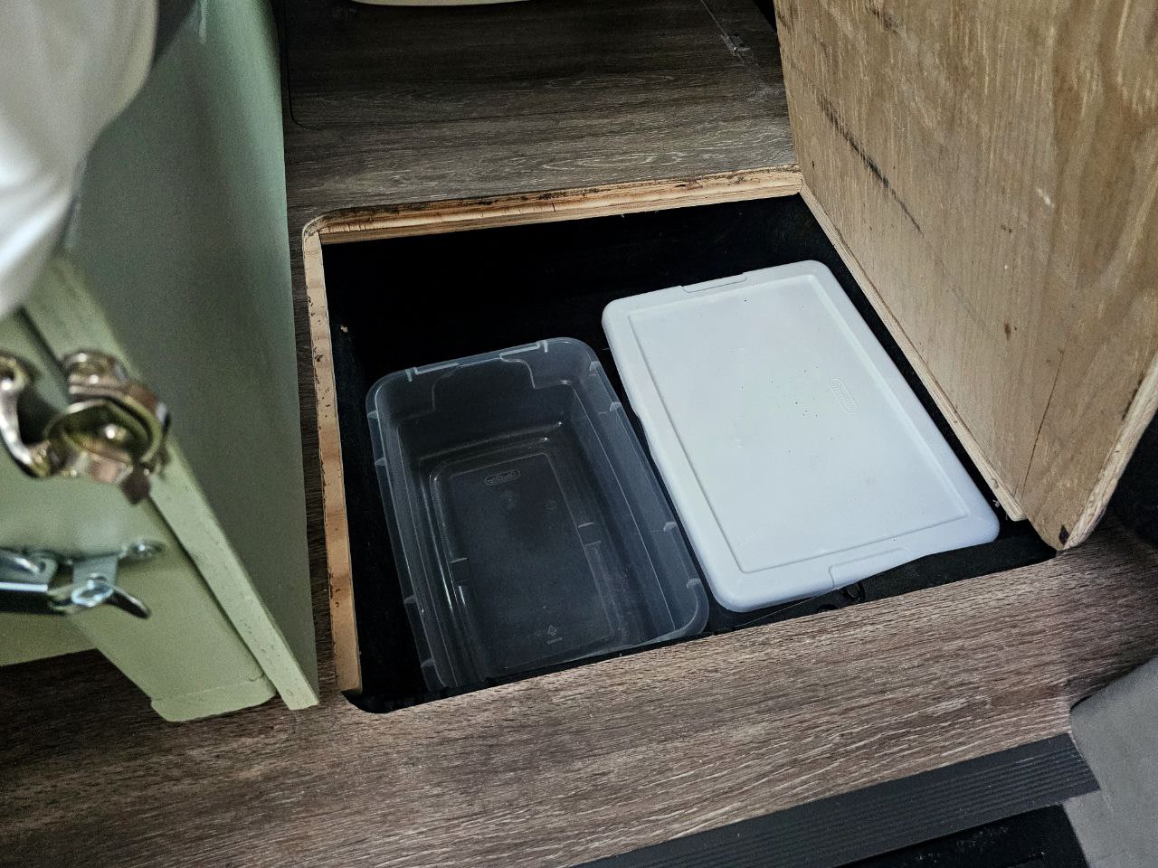 RV rental hidden storage: A convenient floor compartment contains clear and white plastic bins.