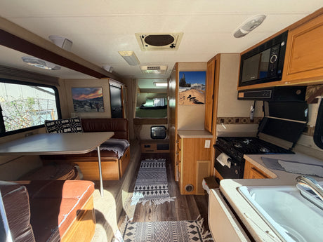 This inviting rv rental interior showcases a full kitchen, dinette, and cozy sleeping area, perfect for travel adventures.