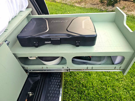 This RV rental features a pull-out camping kitchen with a Coleman stove, pan, and containers, ideal for outdoor cooking.