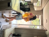 Woman in denim shorts sips from a mug inside a well-equipped rv rental kitchen.