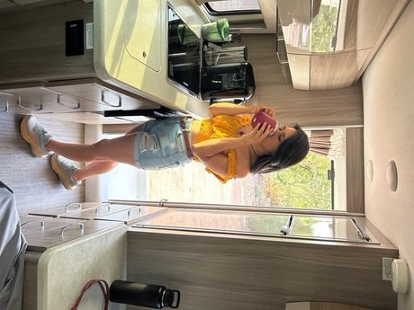 Woman in denim shorts sips from a mug inside a well-equipped rv rental kitchen.