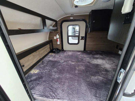 Spacious RV rental interior featuring a large bed with overhead storage and main entry door.