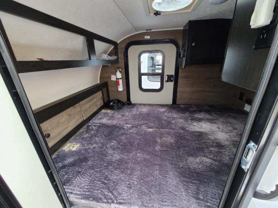 Spacious RV rental interior featuring a large bed with overhead storage and main entry door.