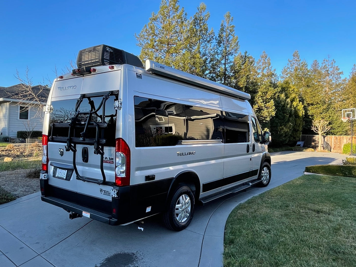 A shiny silver Thor Tellaro camper van, ideal for rv rental, parked on a sunny driveway, featuring rooftop AC and bike rack. — photo 4