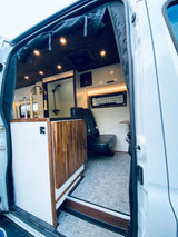 Explore this modern RV rental's interior: a custom camper van featuring a full kitchen, shower, and comfortable seating.