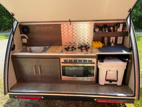 RV rental: Compact outdoor kitchen with a sink, stove, microwave, & cooler for versatile camping meal prep.