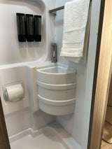 Compact RV rental bathroom featuring a corner sink, mounted soap dispensers, and towel rack with a white towel.