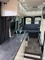 Spacious, modern RV rental interior with a sleek kitchen, comfy seating area, bright lighting, and an AC unit.