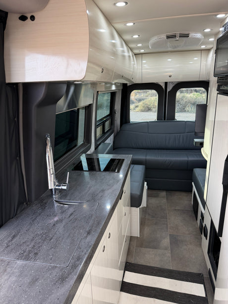 Spacious, modern RV rental interior with a sleek kitchen, comfy seating area, bright lighting, and an AC unit.