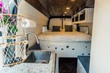 Modern RV rental features a cozy bed, fully equipped kitchen with sink, and smart storage solutions for travel.