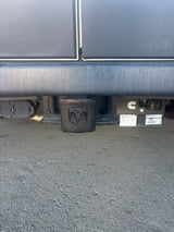 Rear view of an RV rental's trailer hitch with a Ram logo cover, trailer wiring connector, and a Cummins generator.