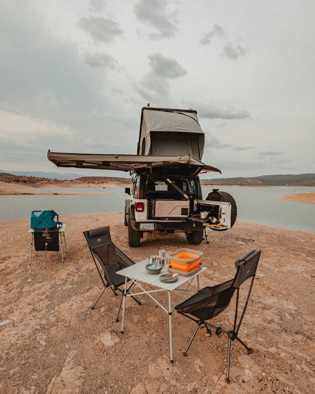 Explore by lake with this overlanding Jeep rv rental, featuring a rooftop tent, awning, and full camp kitchen setup.