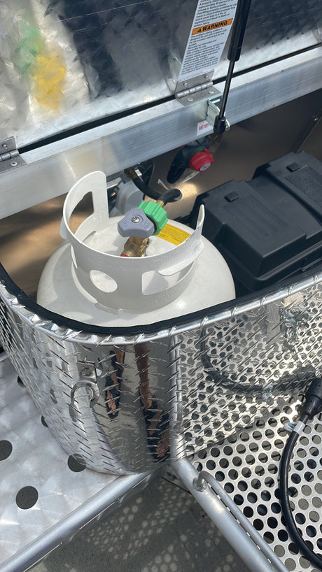 RV rental: A propane tank and battery box within a metal utility compartment with a warning label.