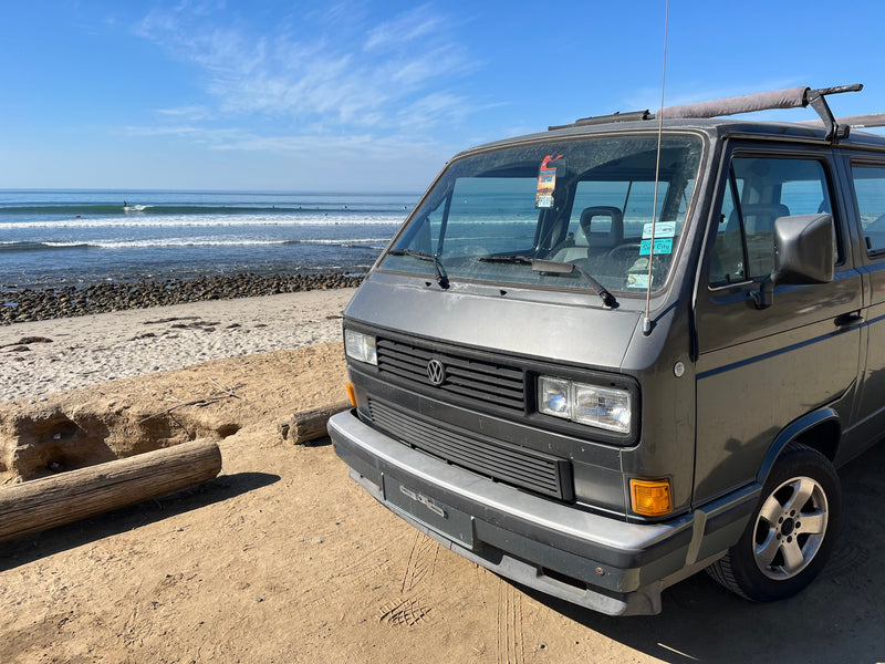 A gray VW camper van, ideal for RV rental, parked on a sunny beach by the ocean with waves and surfers in the distance. — photo 7