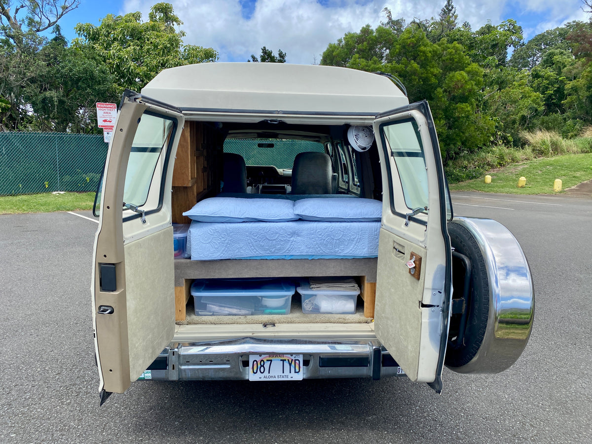 RV rental campervan in Hawaii, rear doors open revealing a cozy bed, fan, and storage bins for van life adventures. — photo 12