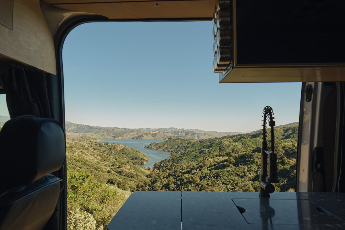  gazing from orange bedding out to sunlit trees from the custom-built van.|Cozy RV rental bed with warm orange bedding — photo 7