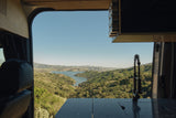 Scenic lake and green hills from an RV rental van, showing an interior counter and faucet.