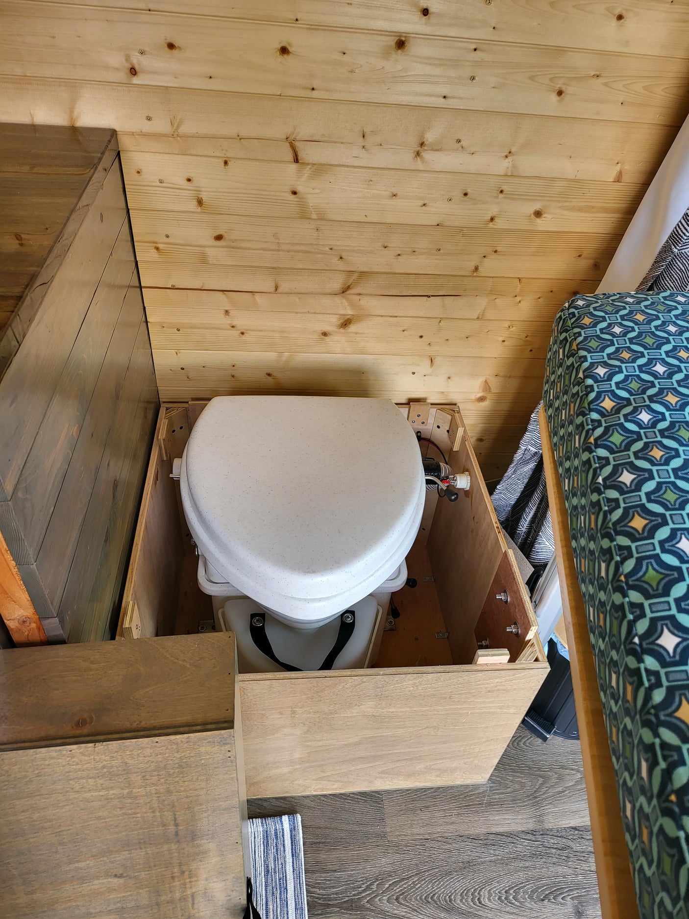 Compact composting toilet storage in an RV rental interior, showing wooden walls and flooring.