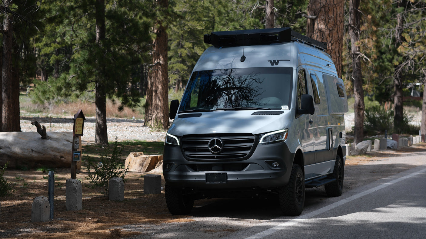 Experience nature with this Winnebago Revel RV rental, a Mercedes Sprinter camper van, parked in a sunlit forest campsite.