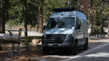 Experience nature with this Winnebago Revel RV rental, a Mercedes Sprinter camper van, parked in a sunlit forest campsite.