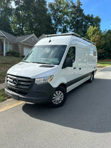 White Mercedes Sprinter camper van for RV rental. Features roof solar panels and a dark lower body.