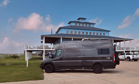 Dark gray Noovo rv rental van parked at a large blue building. Explore travel & vacation possibilities.