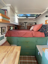 Cozy RV rental interior featuring a comfy bed, green storage, and wooden surfaces for your adventure.