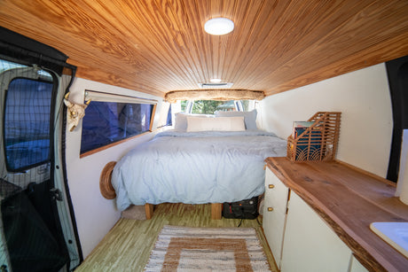 Cozy rv rental interior with a light blue bed, wooden ceiling, and ample storage, perfect for a comfortable road trip.