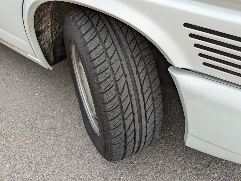 Close-up of a white RV rental's front passenger wheel, tire tread, and fender with horizontal vents. — photo 17
