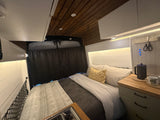 Cozy RV rental interior: a comfy bed, warm wood ceiling, functional kitchen with shiplap walls & smart storage solutions.