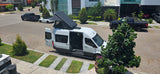 Overhead of a white camper van with a raised pop-top tent & open doors on a sunny street. Perfect for an rv rental adventure!