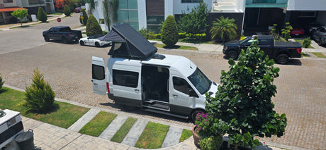 Overhead of a white camper van with a raised pop-top tent & open doors on a sunny street. Perfect for an rv rental adventure!