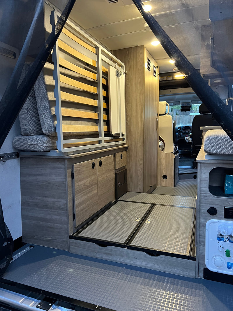 Explore this modern RV rental interior, showcasing sleek cabinetry, a convertible bed, and clever storage in this camper van conversion. — photo 11