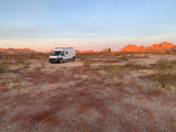 White RV rental parked in a vast desert with orange mountains at golden hour. Ideal for remote camping.