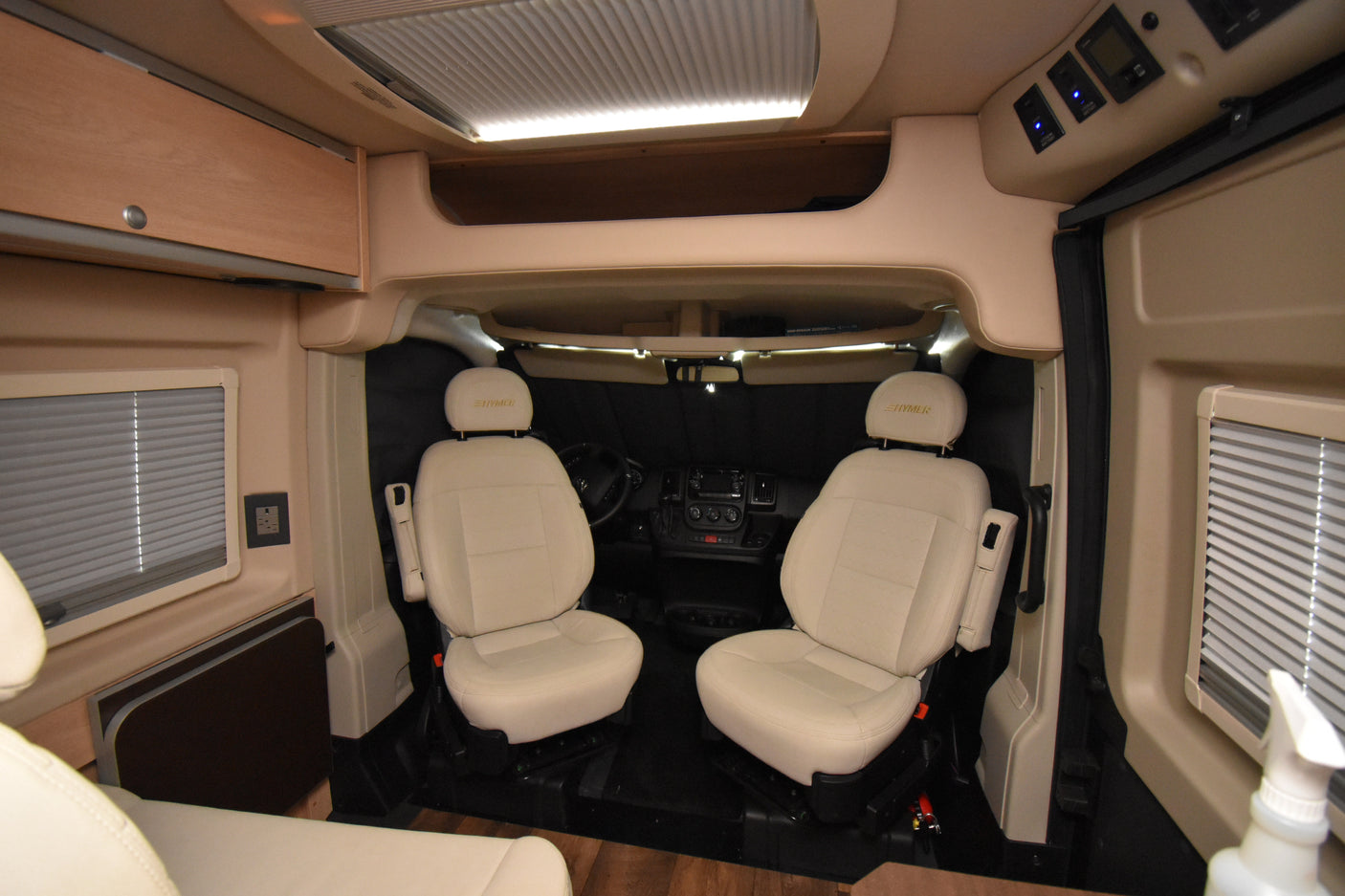 Modern camper van interior with cream HYMER front seats, driver's cabin view, and overhead storage, perfect for your rv rental.