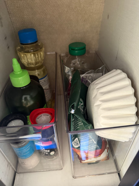 Organized pantry staples in clear bins, ideal for compact RV rental kitchen storage: coffee, spices, and oils.