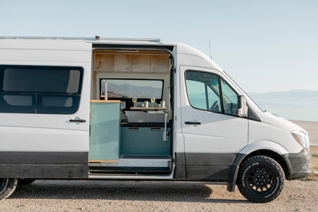 White Sprinter RV rental by a lake, showcasing its cozy, customized interior for adventure travel and van life.