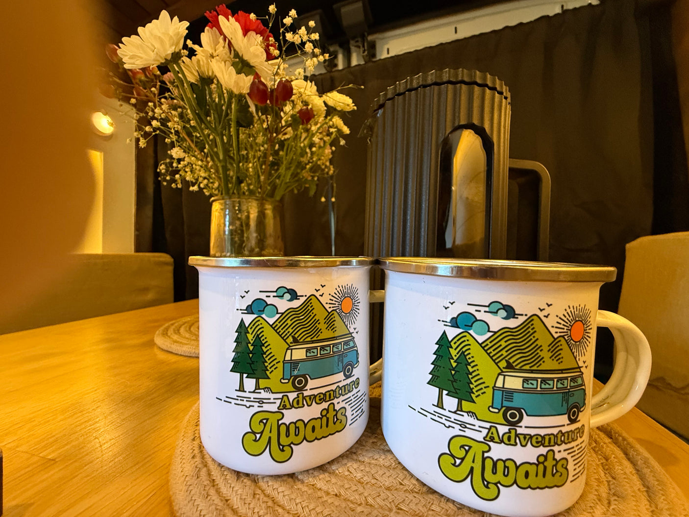Enamel "Adventure Awaits" mugs & fresh flowers create a cozy scene in an RV rental, ready for travel and adventure.