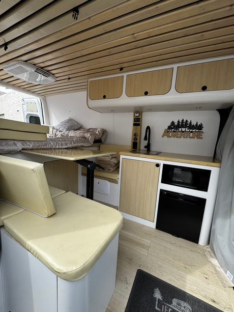 This RV rental interior features a comfortable bed, compact kitchen with sink, microwave, fridge, and a versatile dining area.