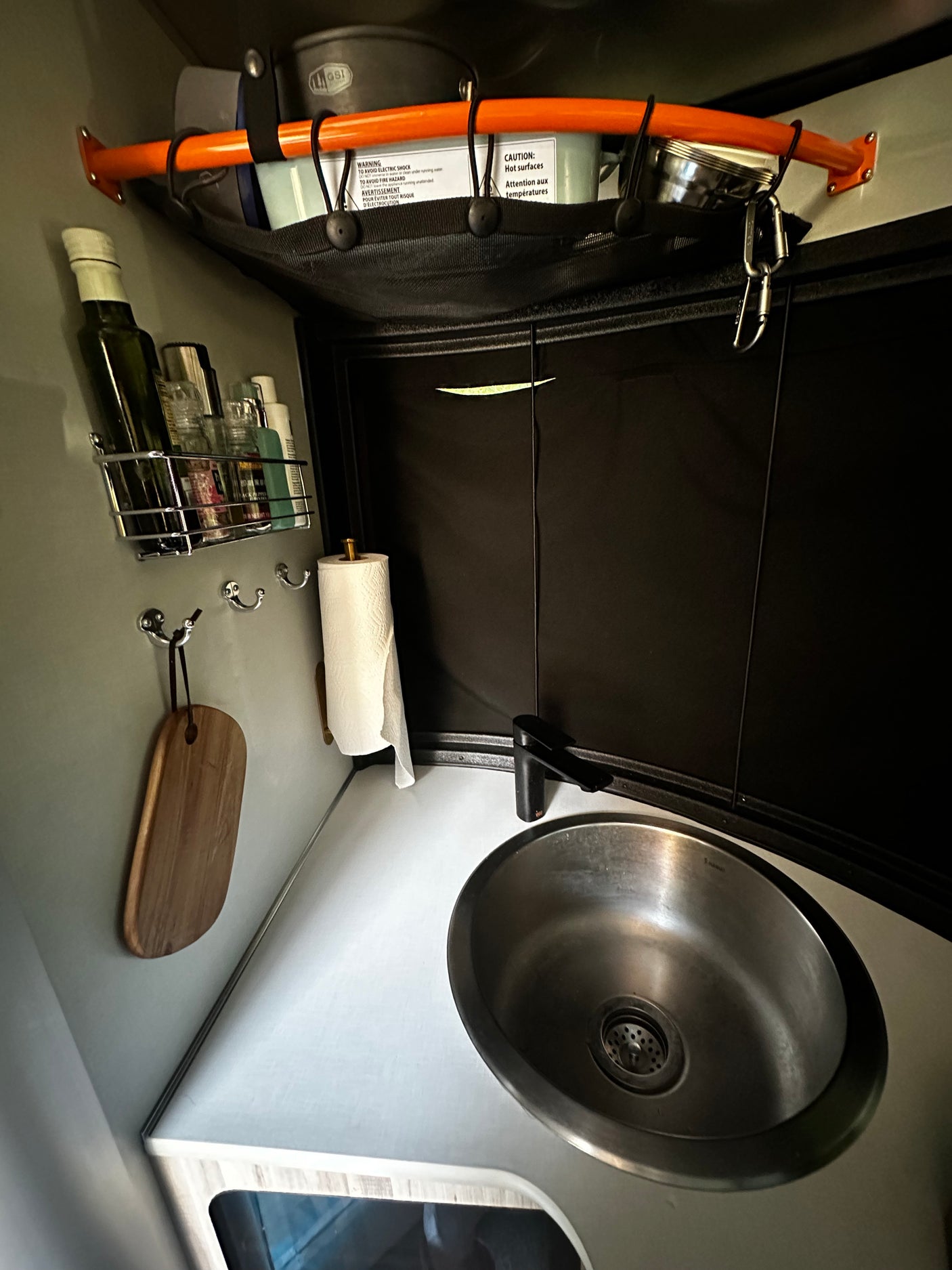 RV rental compact kitchen with sink, overhead mesh storage for cookware, & wall-mounted spice rack. Ideal for travel.