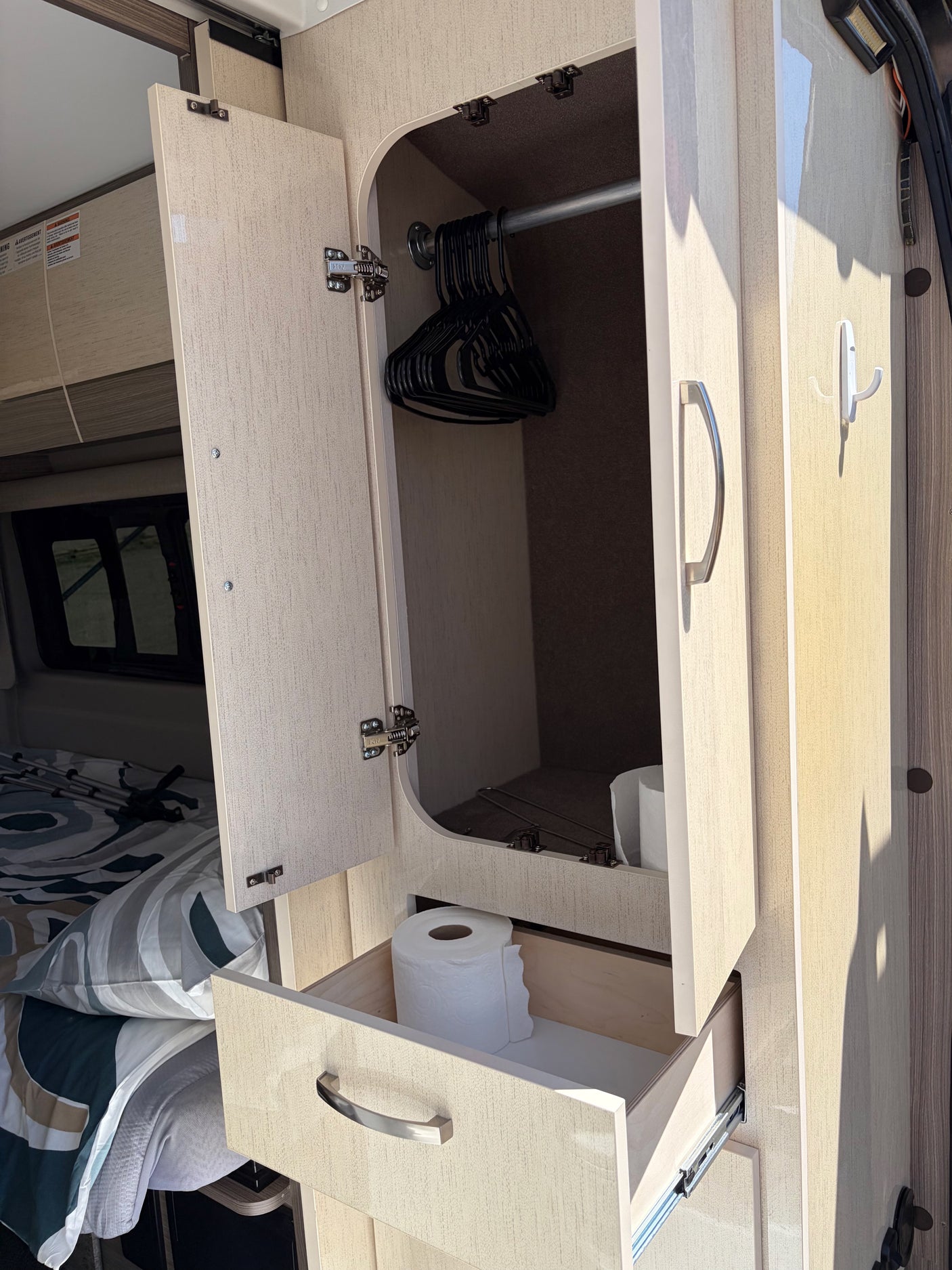 RV rental interior: open closet with hangers, drawer with toilet paper, & bed. Compact storage solutions for travel.