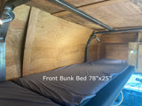 Interior view of an RV rental showing a comfy 78x25-inch front bunk bed with wood paneling and lighting.