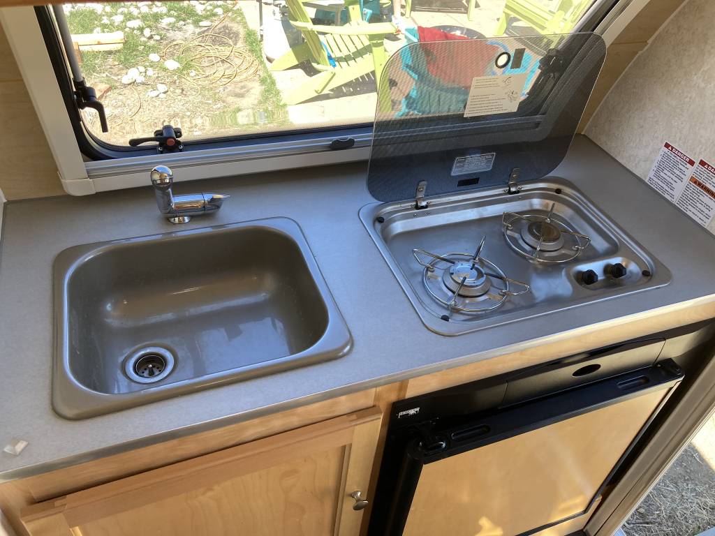 This RV rental kitchenette features a compact sink, 2-burner stove, and under-counter refrigerator, ideal for travel. — photo 4