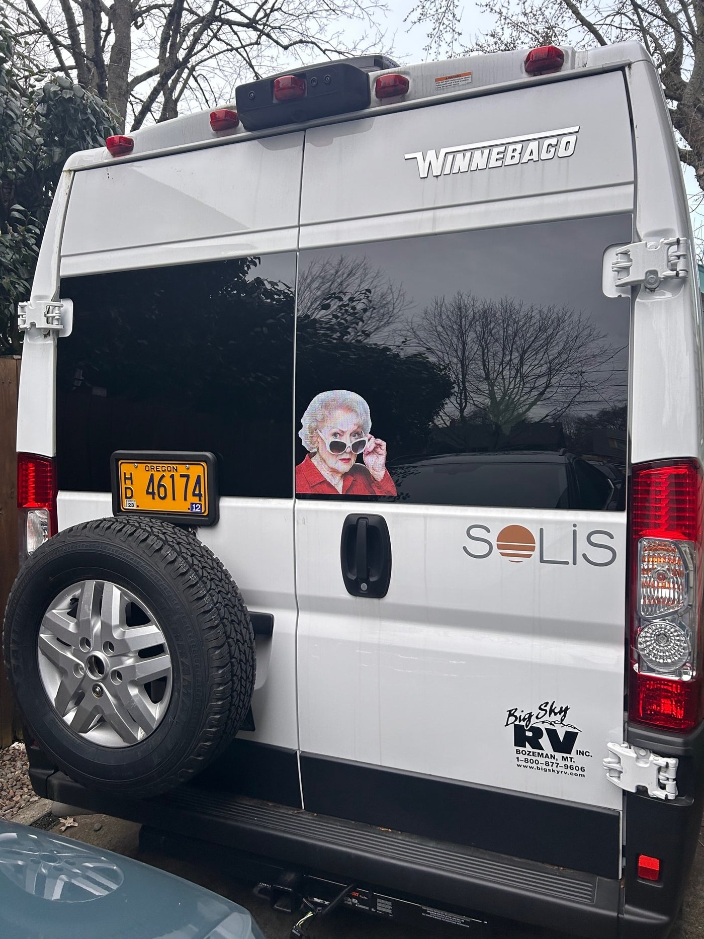  holding a "Welcome" sign.|White Winnebago Solis RV rental at a sunny campsite — photo 4