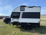 A black and white Go Lite travel trailer, ready for adventure. This RV rental is hitched to a GMC truck on a grassy field.