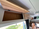 Overhead light wood cabinets in an RV rental offer ample storage. One cabinet open, revealing interior space, with a bright outdoor view.
