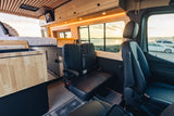 Spacious, wood-paneled RV rental interior with bed, seating, and stunning sunset ocean views from your camper van.