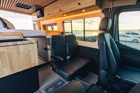 Spacious, wood-paneled RV rental interior with bed, seating, and stunning sunset ocean views from your camper van.