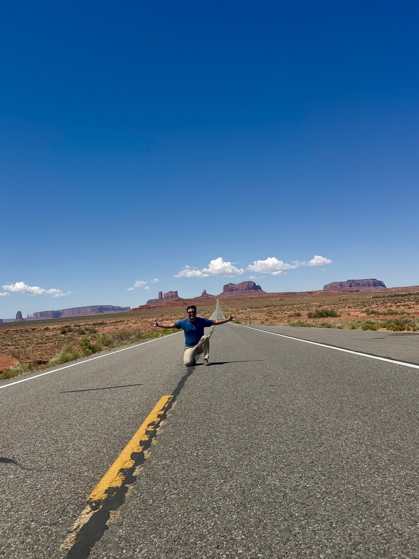 Scenic RV rental trip through Monument Valley! A man kneels on the highway amidst stunning desert mesas. — photo 20