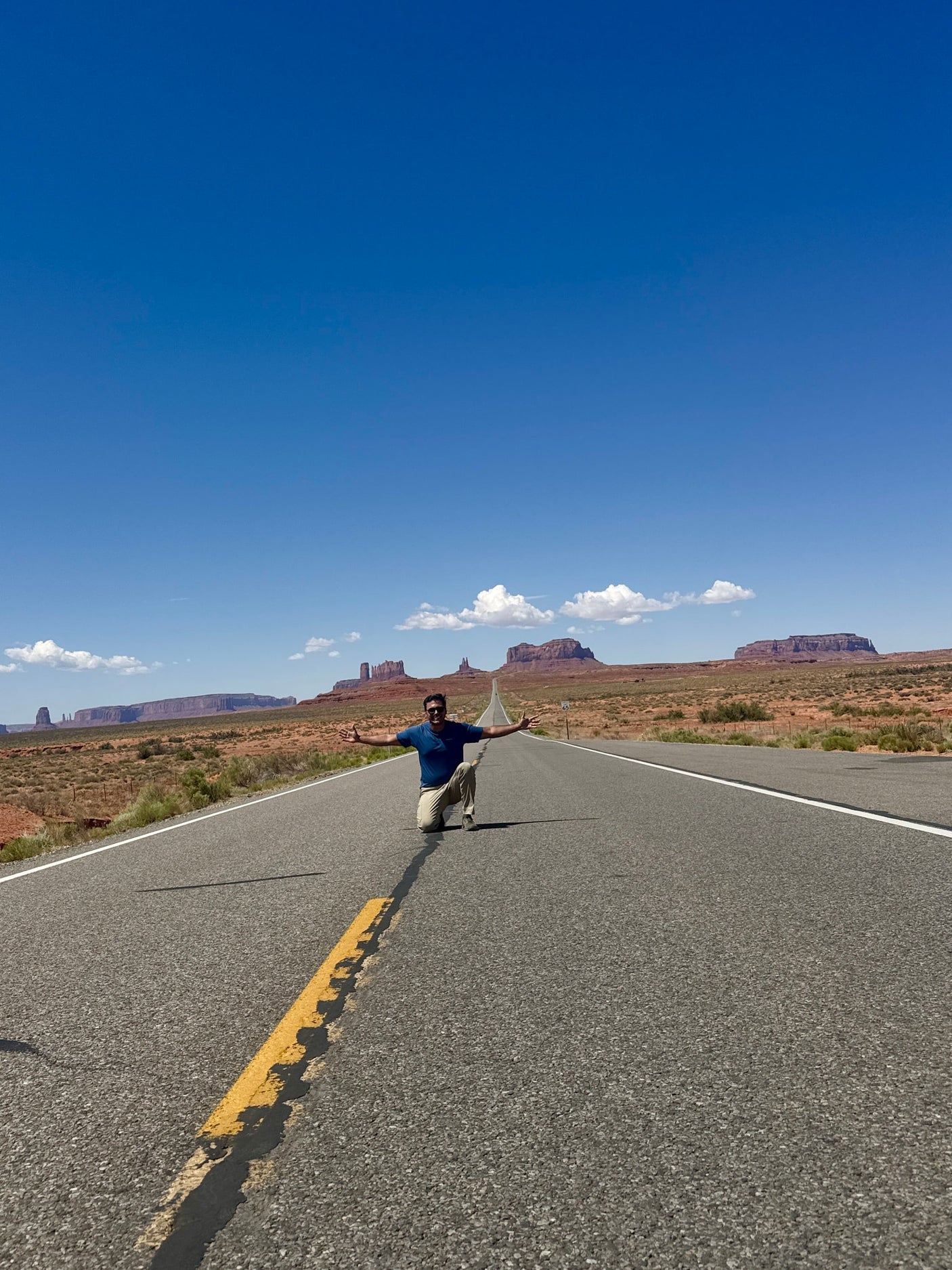 Scenic RV rental trip through Monument Valley! A man kneels on the highway amidst stunning desert mesas.